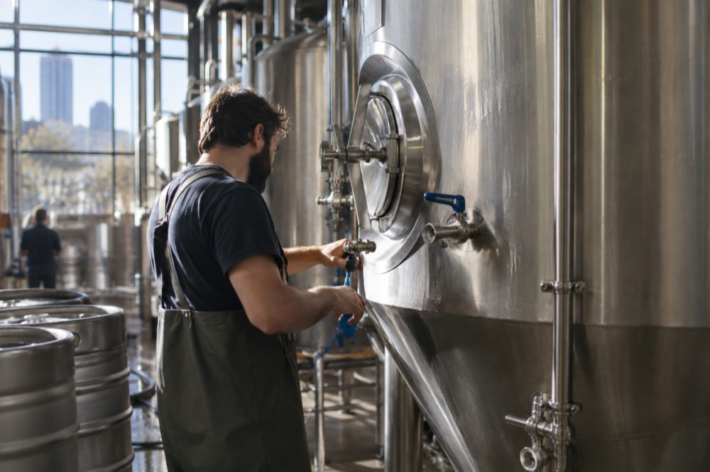 A brewer checking a stainless steel fermentation tank inside a working brewery