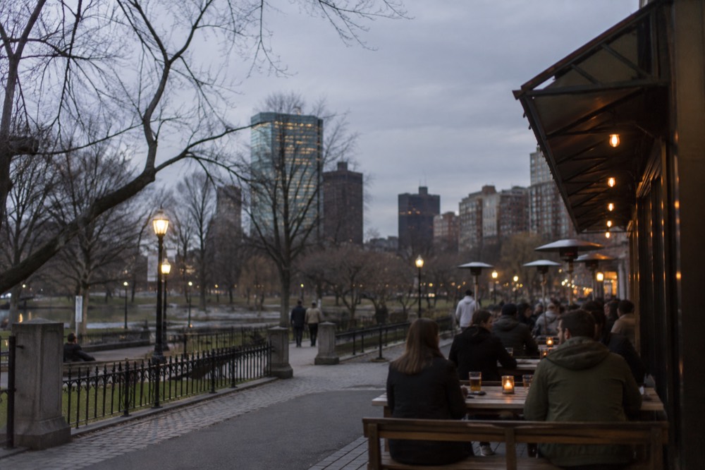 People seated at picnic tables outside a brewery on a city street at dusk