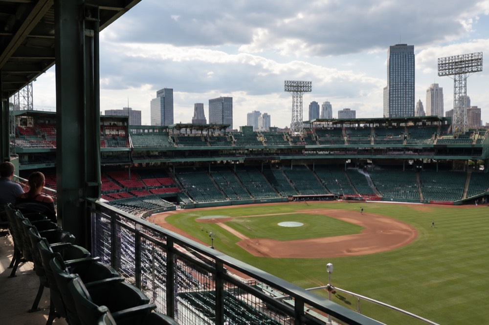 A historic ballpark interior with green seats seen from an upper concourse