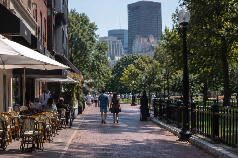A narrow brick street with café awnings and tables set out on the sidewalk in the morning