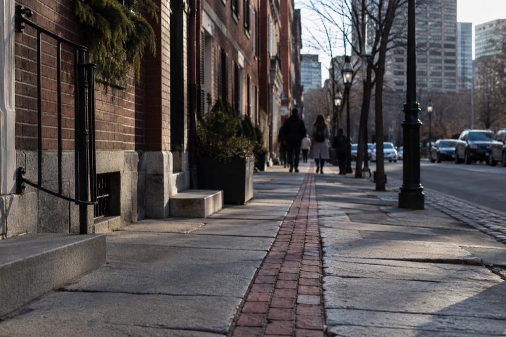 A red-brick Freedom Trail line running along a sidewalk past historic buildings