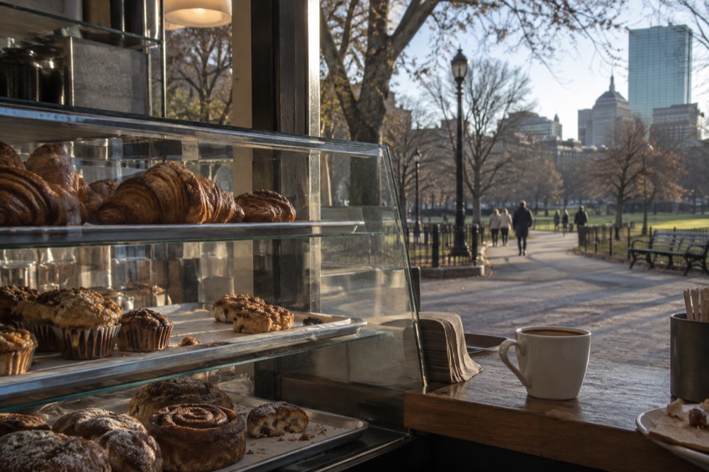 A bakery counter with trays of pastries and a cup of coffee on a wooden surface