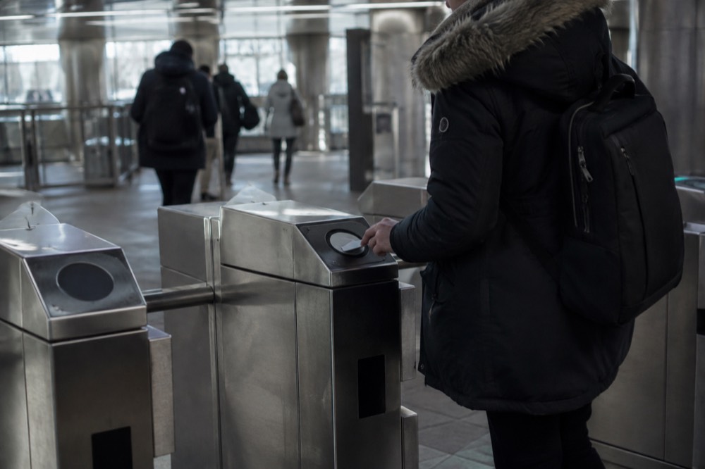 A passenger tapping a contactless card at a subway fare gate in Boston