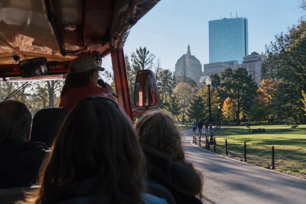 A duck boat driver-guide narrating to passengers with a microphone during the street portion of the tour