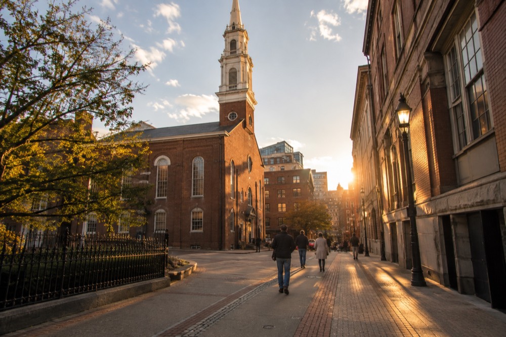 Visitors walking the red brick line of the Freedom Trail past an old church