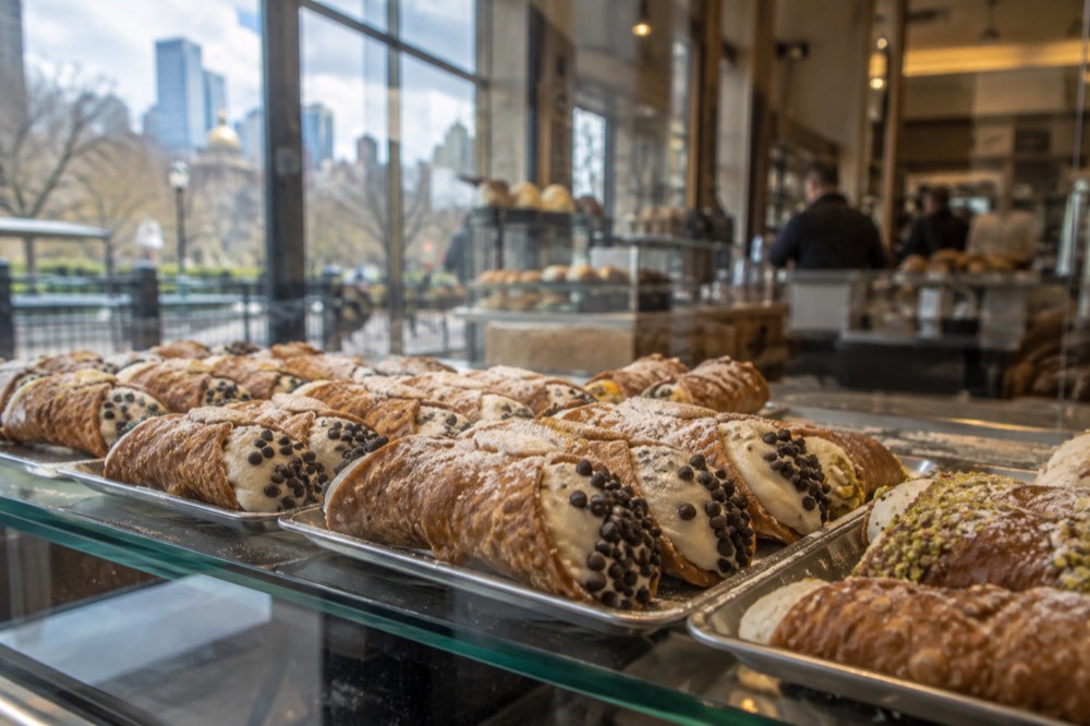 Cannoli pastries arranged in a glass display case at a North End bakery counter