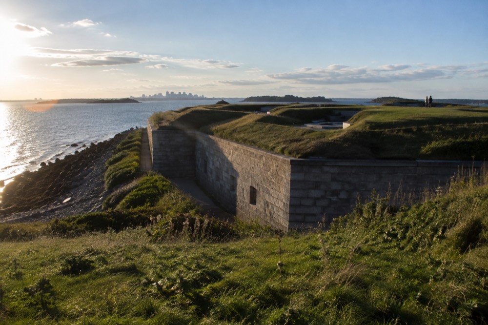 A granite fort with grassy ramparts on a harbor island under a blue sky