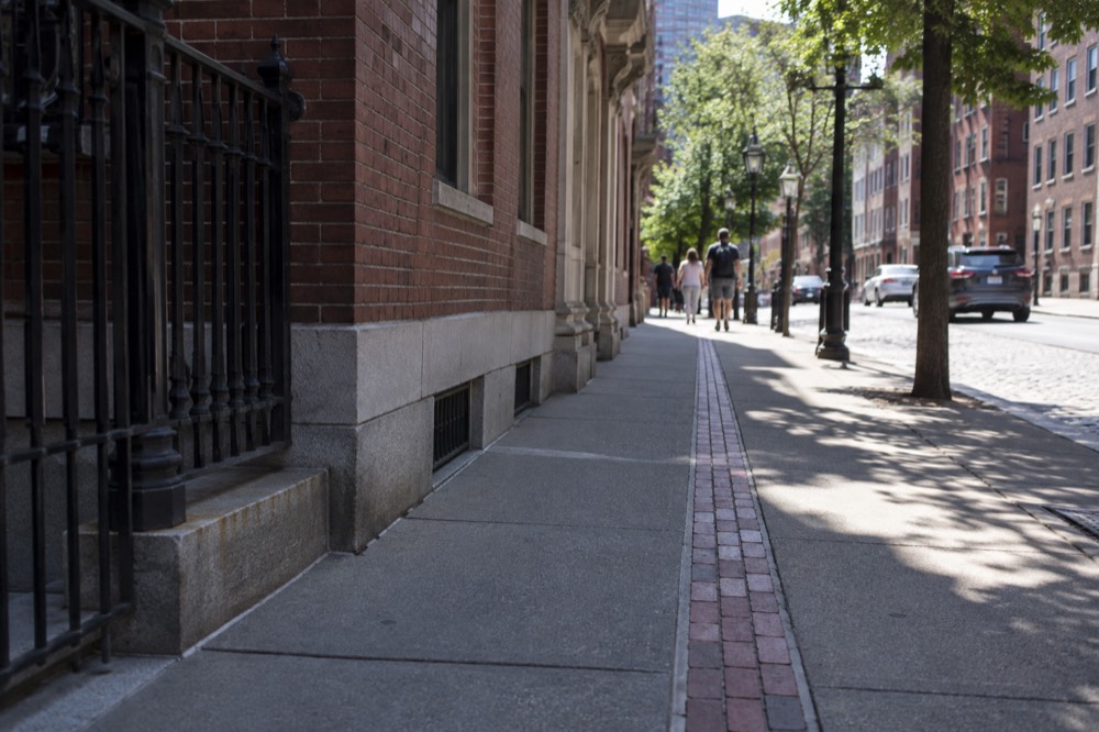 The red brick Freedom Trail line running along a Boston sidewalk past historic buildings