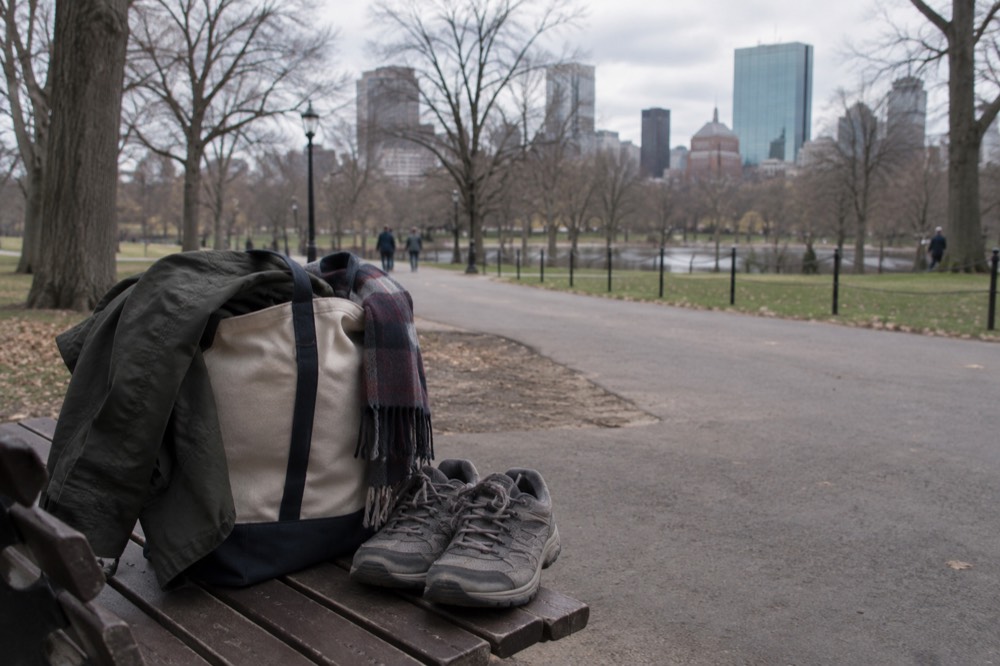 A packed tote bag with a jacket, scarf and walking shoes on a wooden floor