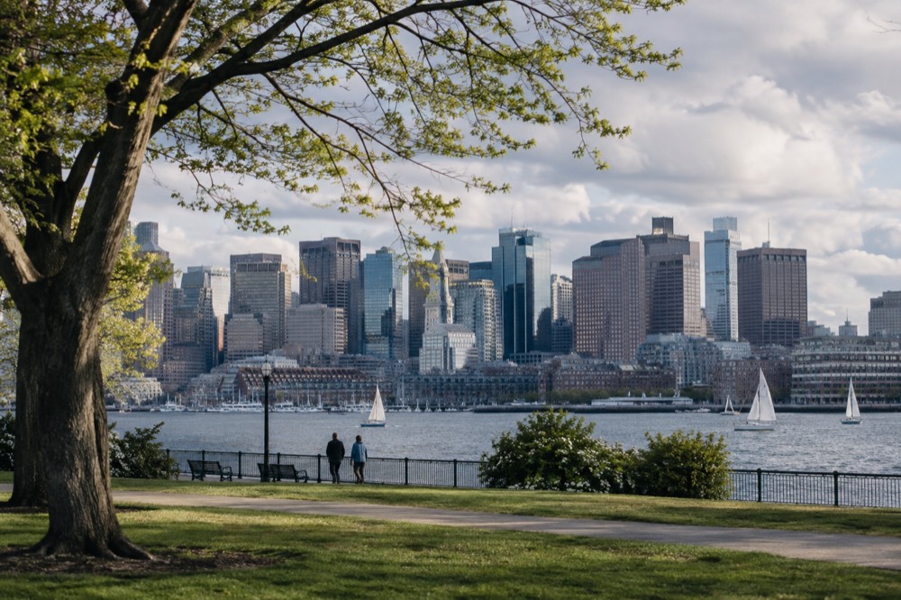 A wide spring view of the Boston skyline and harbor from a waterfront park