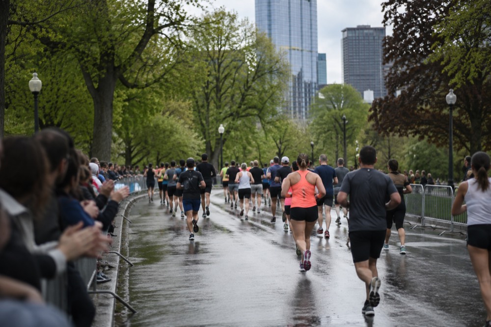 Spectators lean over barricades cheering as a stream of runners passes on a tree-lined street
