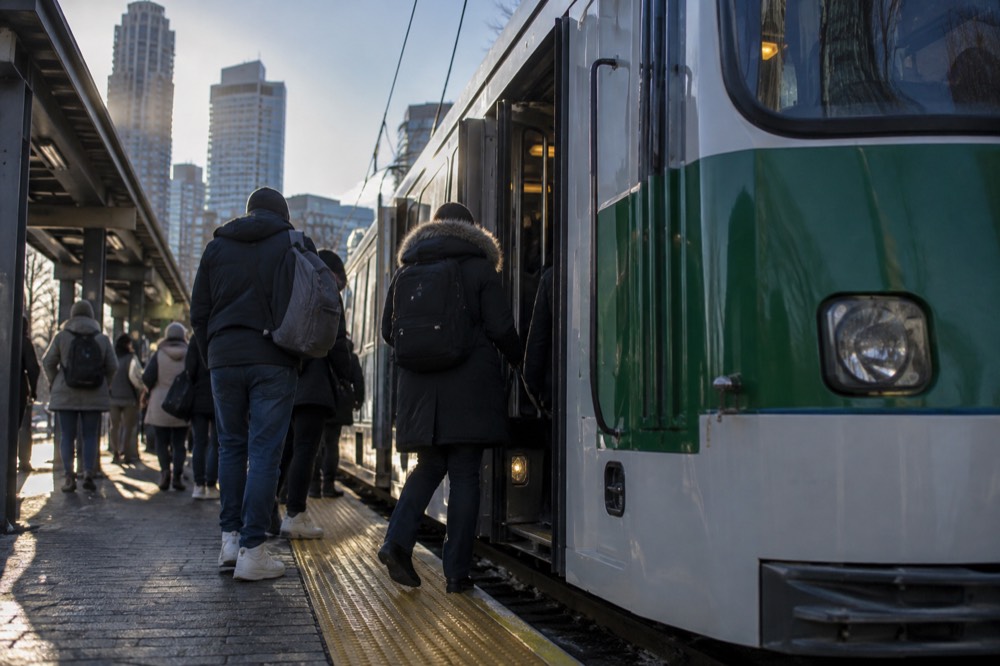 Commuters board a crowded green line train at an outdoor subway station