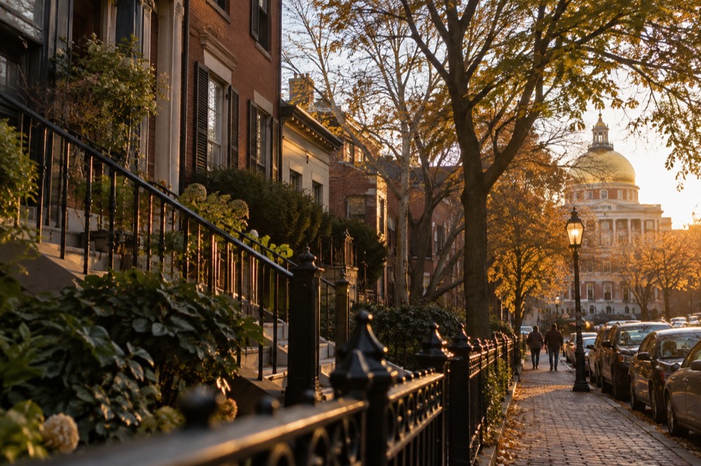 Rowhouses on a tree-lined Boston street with the State House dome visible in the distance
