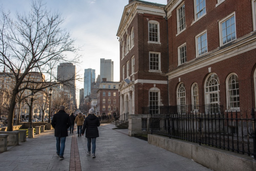 Visitors walking the red brick line of the Freedom Trail past a historic Boston building
