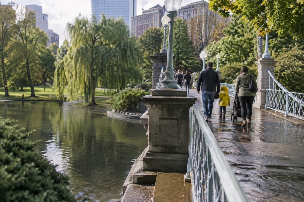 A family walking across a bridge in the Boston Public Garden on a bright afternoon