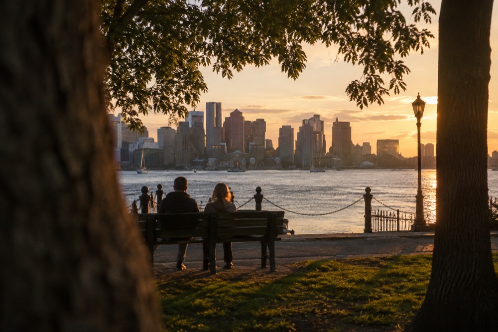 Boston skyline across the harbor at golden hour with waterfront buildings reflected in calm water