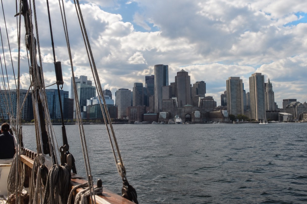 Boston financial district skyline seen across the harbor from a boat with a sailing ship rigging in the foreground