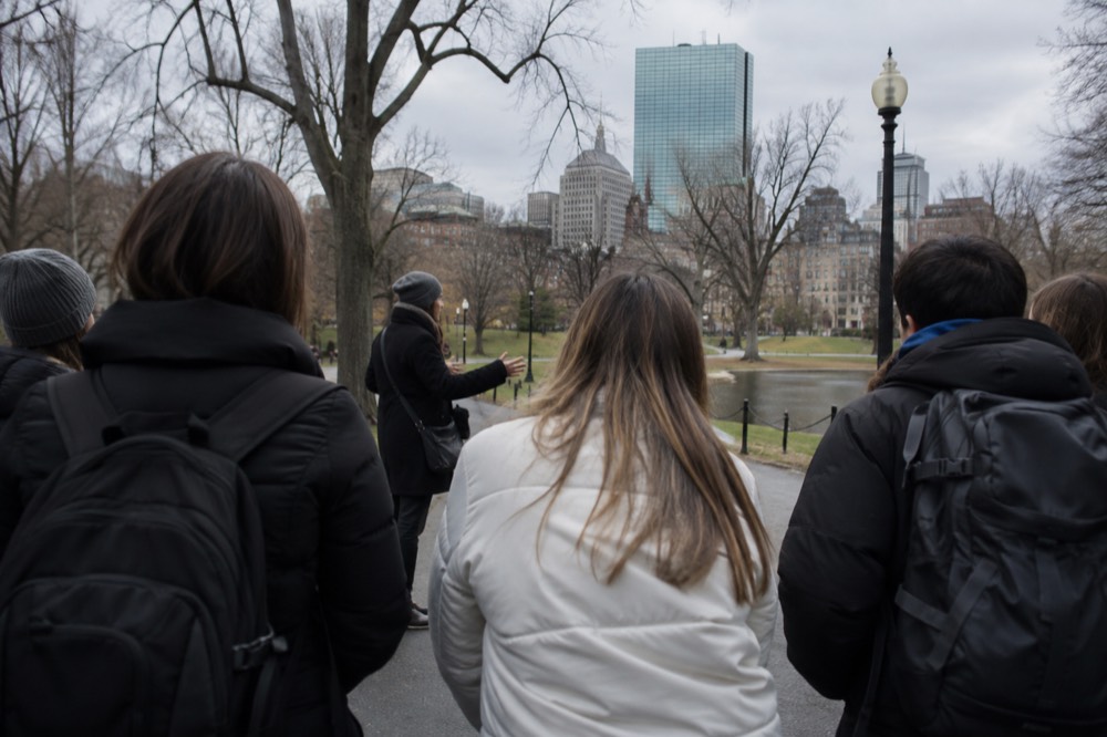 A tour guide speaking to a small group holding maps on a Boston sidewalk