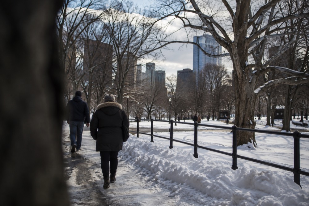 Snow piled along a Boston sidewalk with pedestrians walking carefully