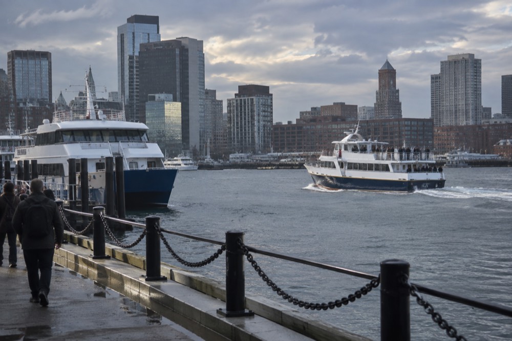 A whale watching boat heading out from a Boston harbor dock past a ferry