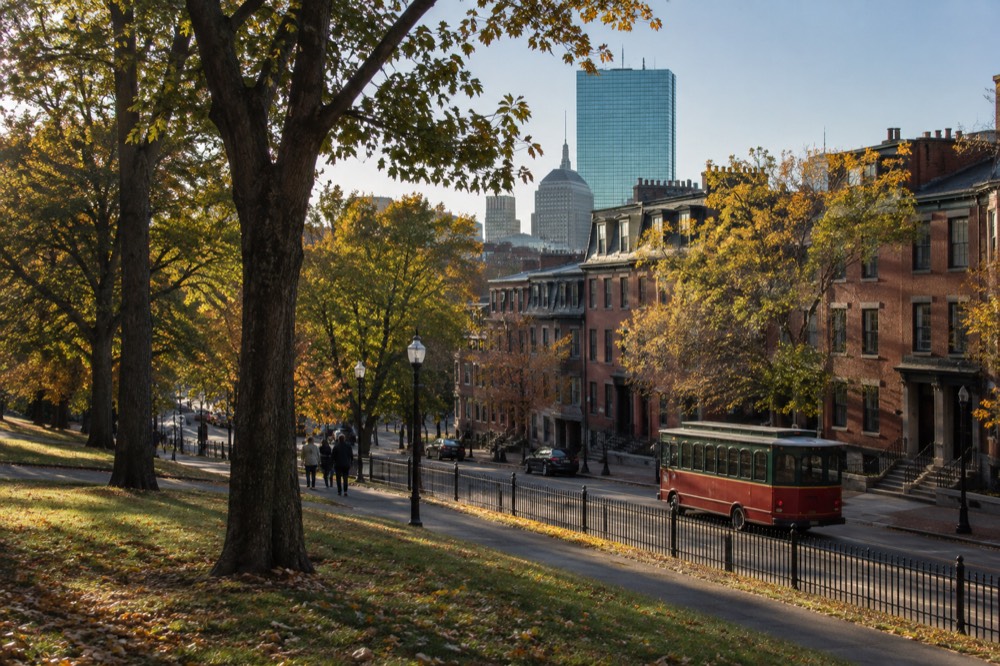 An open-air red sightseeing trolley traveling past brick rowhouses on a Boston street