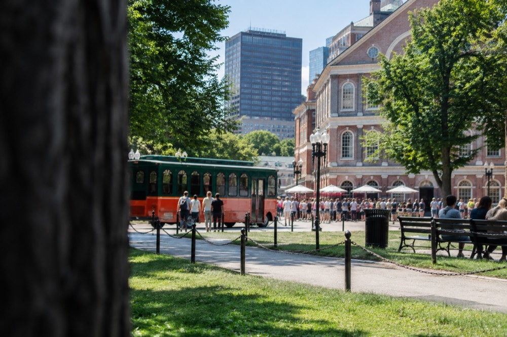 A sightseeing trolley parked near a historic brick marketplace with crowds on the sidewalk