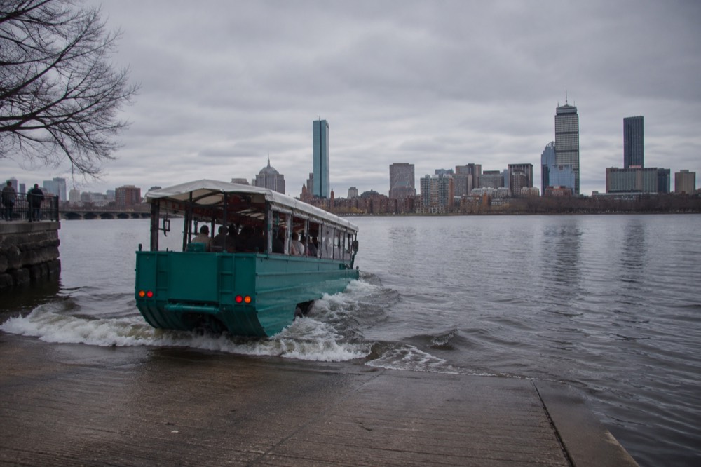 An amphibious duck boat entering the Charles River with the Boston skyline behind it