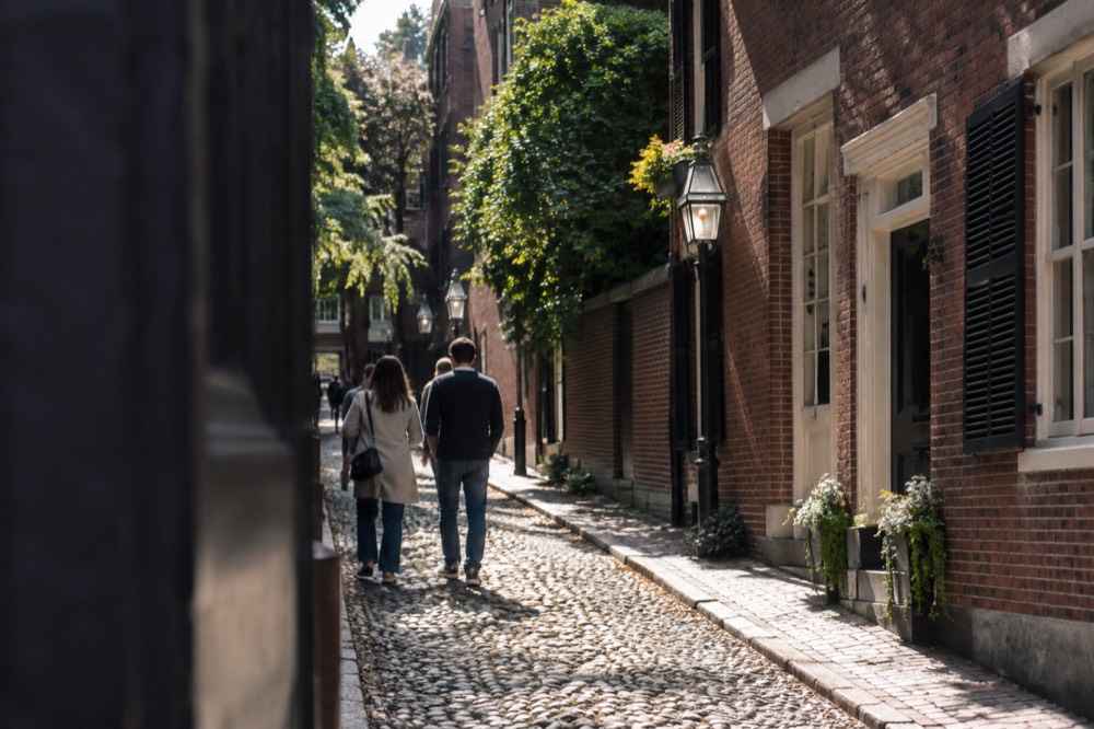 Visitors walking a narrow cobblestone lane between old brick buildings in downtown Boston
