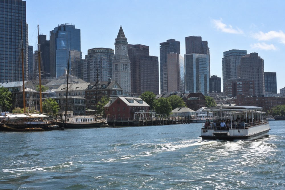 A sightseeing boat cruising past a historic waterfront with masted ships at their docks