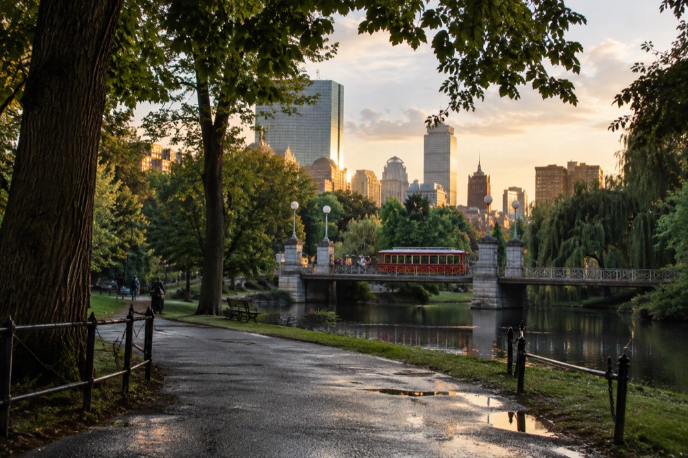 A red trolley crossing a bridge with the Boston skyline in golden evening light