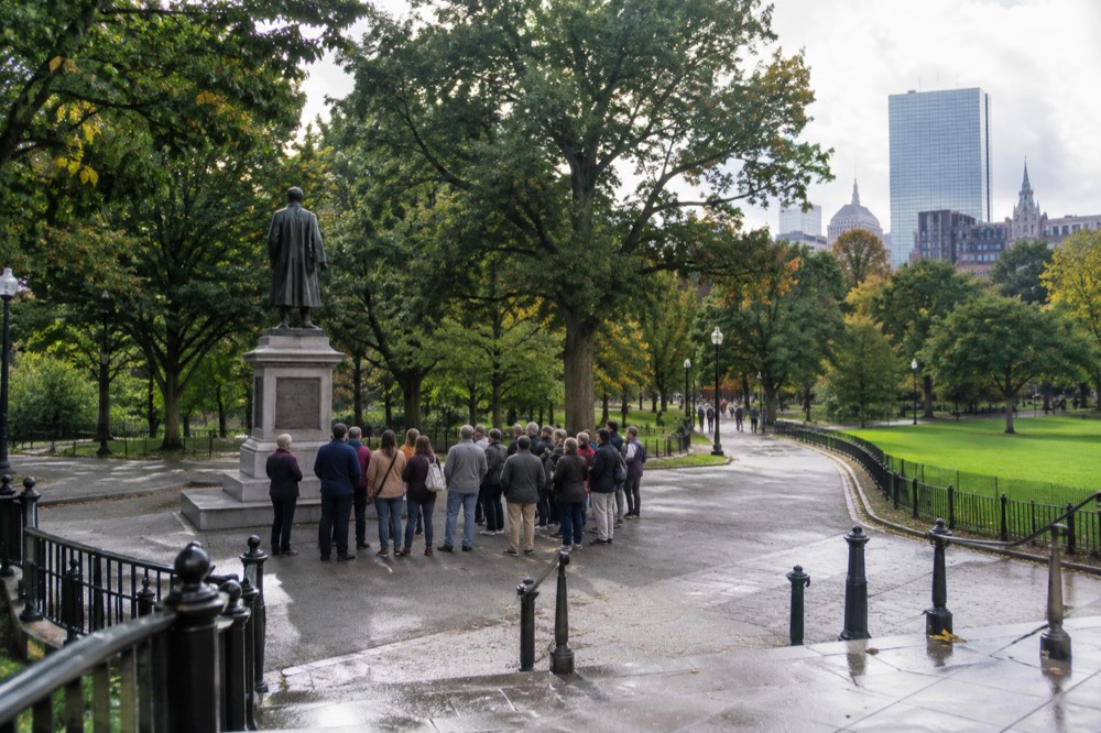 Tour group gathered around a guide near a historic campus statue