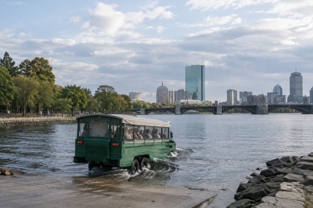 Amphibious tour vehicle entering a river beside a city skyline
