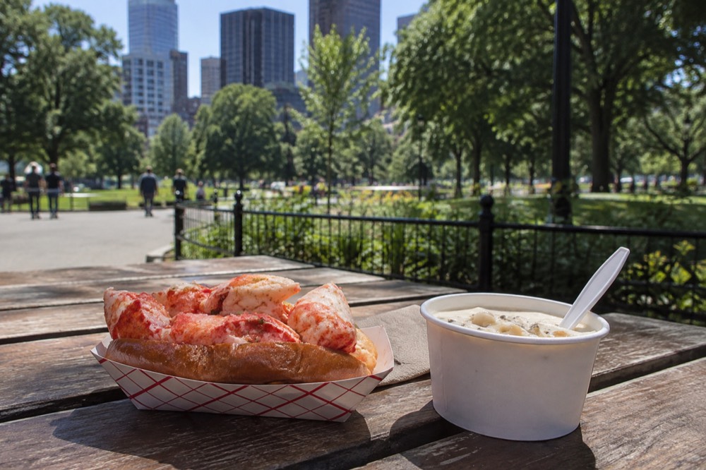 A lobster roll and a cup of clam chowder served on a wooden table
