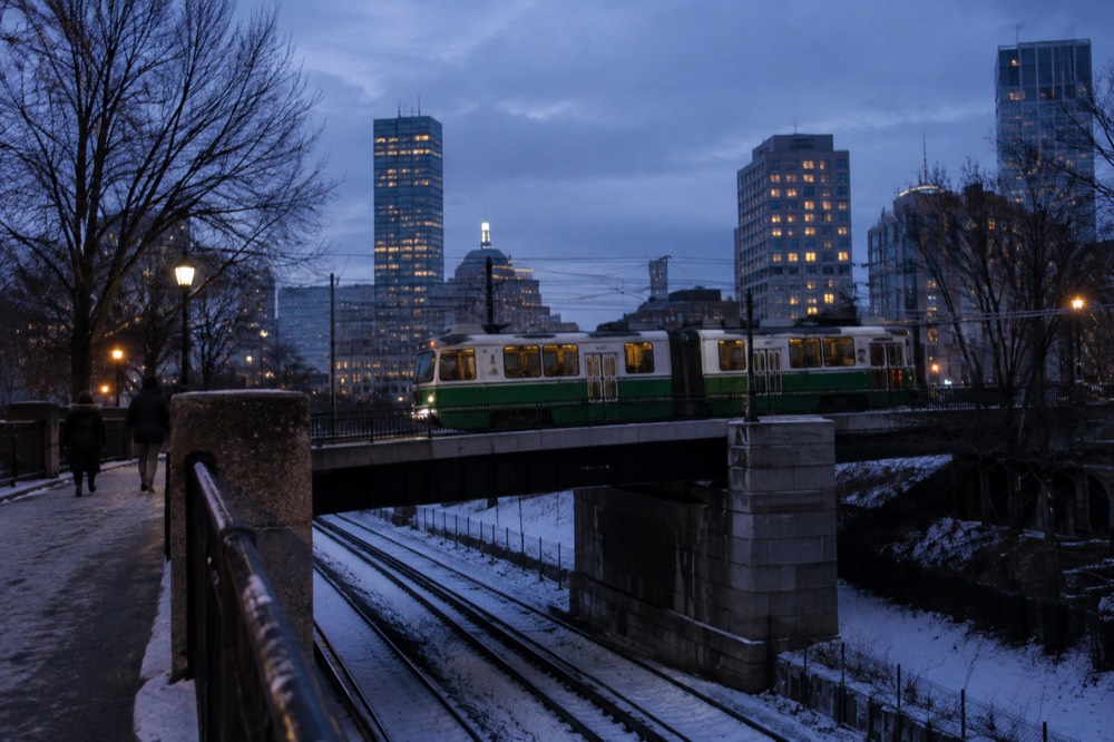 A Green Line trolley crossing a bridge over snow-dusted tracks