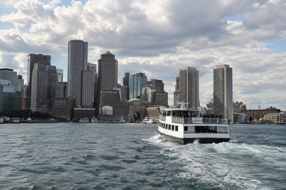 A sightseeing boat moving across Boston Harbor with the downtown skyline behind it