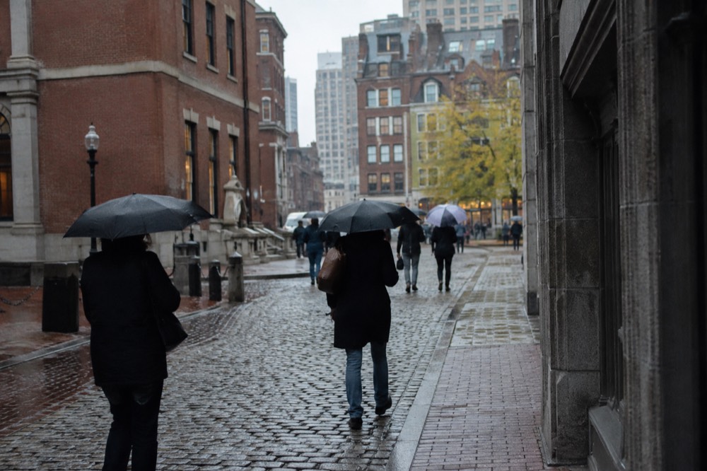 Umbrella-carrying pedestrians crossing a wet cobblestone street in downtown Boston