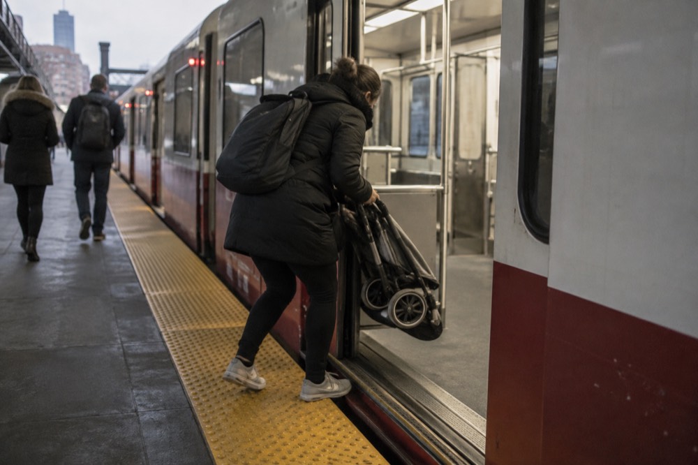 A parent folding a stroller while boarding a modern subway train at a Boston station