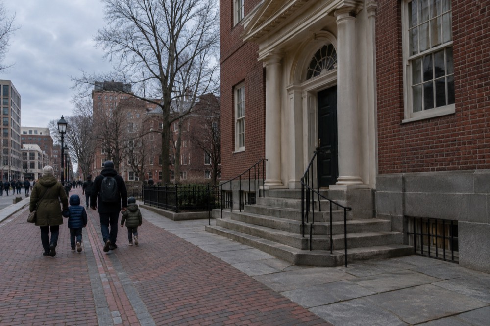 A family walking the red brick line of the Freedom Trail past a historic Boston building
