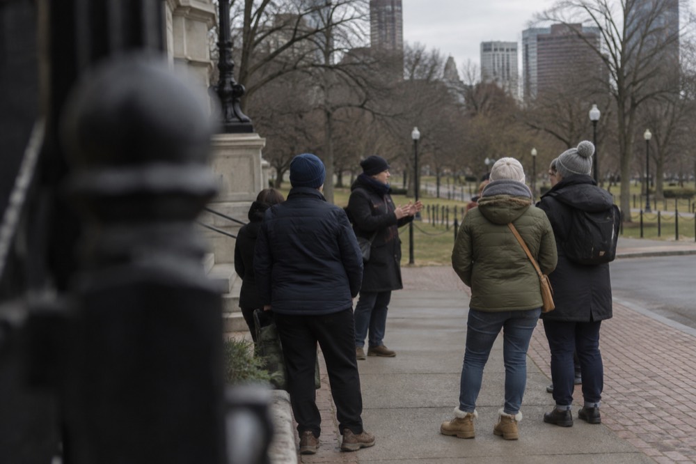 A tour guide speaking to a small group on a Boston sidewalk near historic buildings