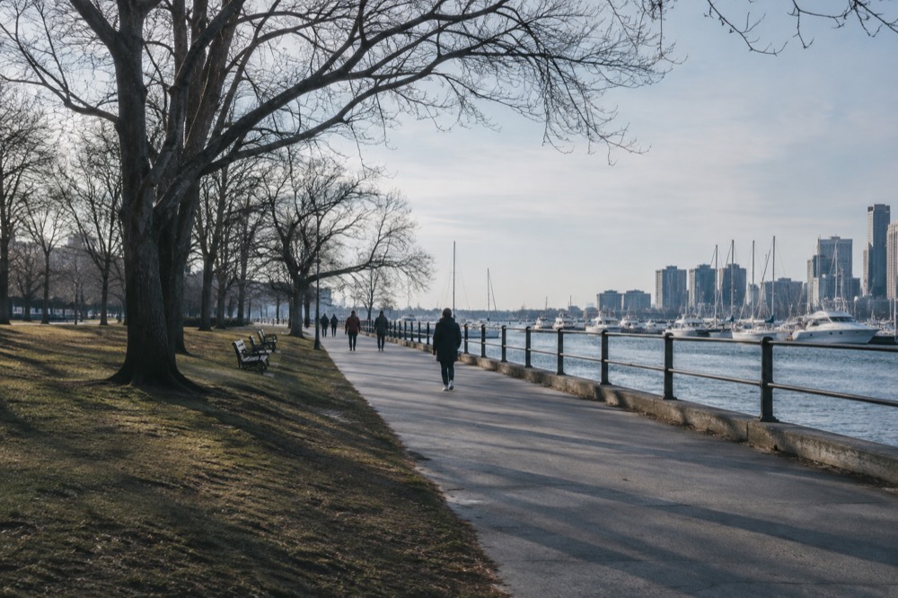 A wide public path along Boston's waterfront with boats moored in the harbor
