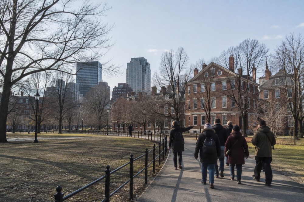 A tour guide leading a small group past historic brick buildings in Boston