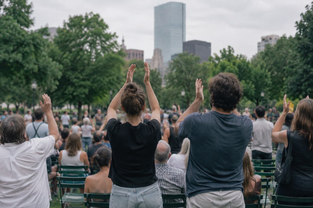 A crowd of fans cheering behind rows of green seats on a summer afternoon