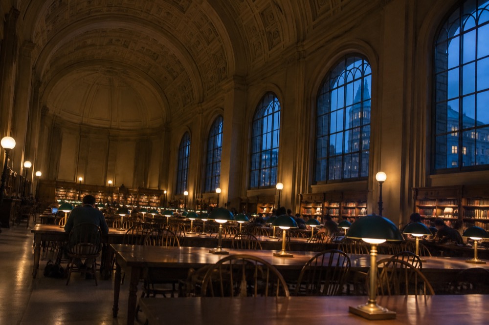 The long reading room of the Boston Public Library with arched windows and rows of desks