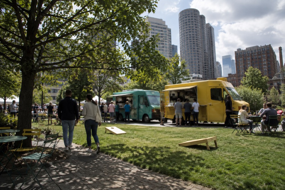 People strolling past food trucks and lawn games on the Rose Kennedy Greenway