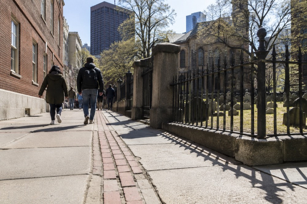 Visitors walking along a red brick line past a historic Boston burying ground