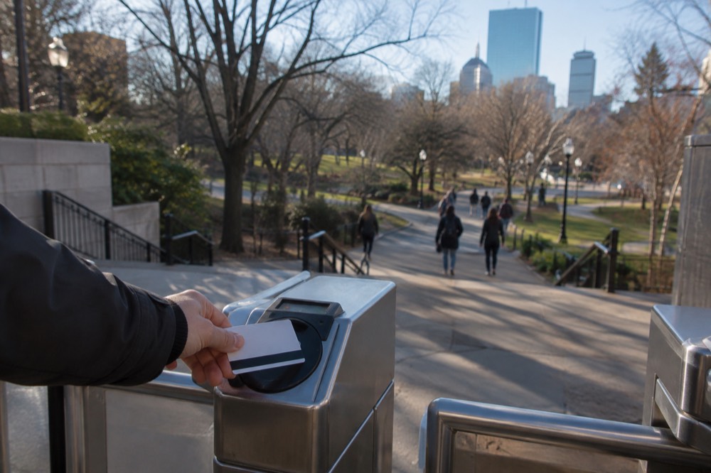 A hand tapping a fare card at an MBTA station entrance