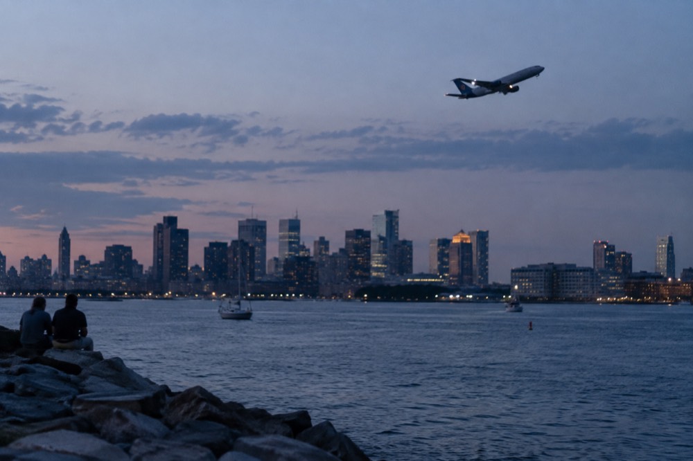 An airplane ascending over Boston harbor with the city skyline in the distance at dusk