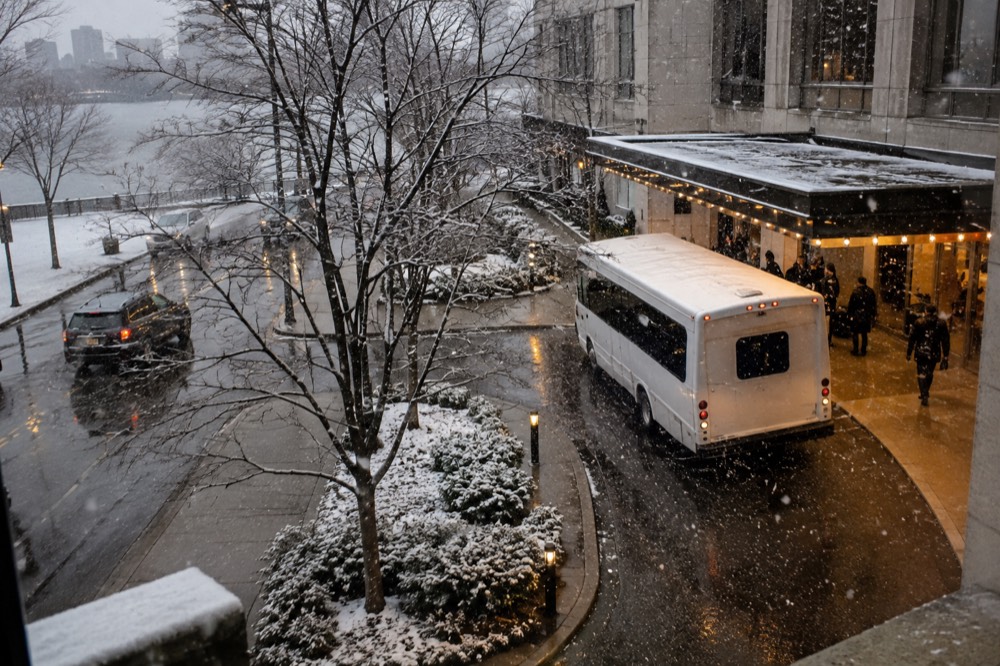 Snow falling on a hotel entrance with a shuttle bus waiting under awning lights