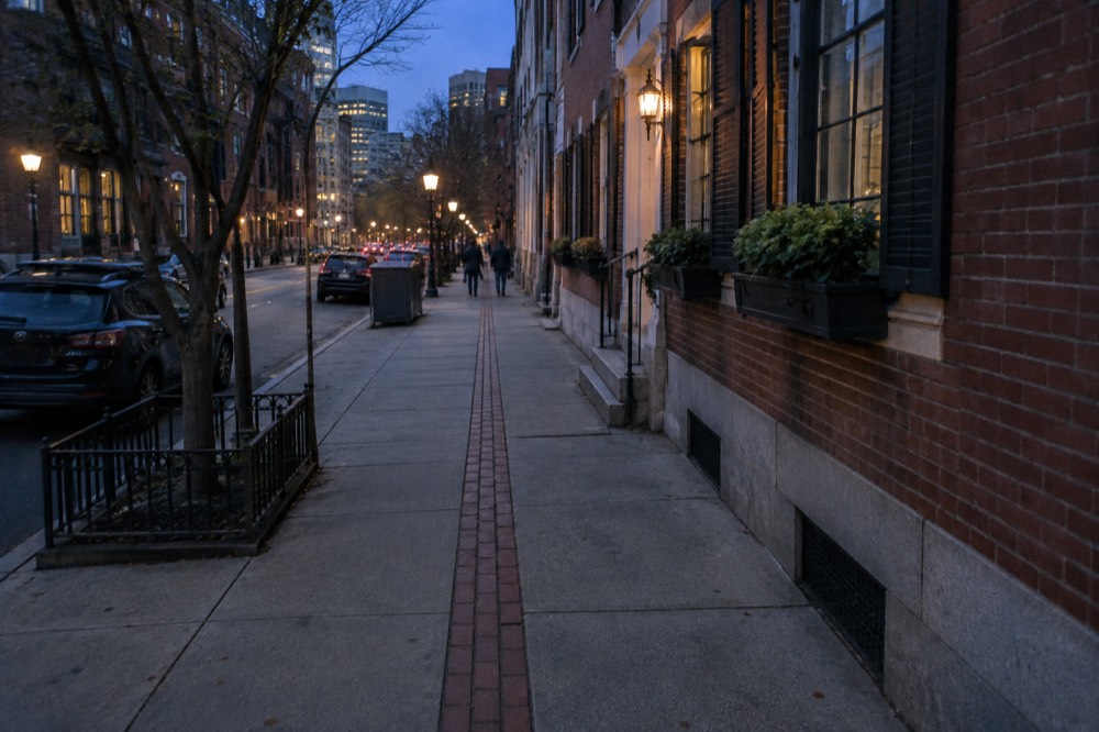 A red brick line marking the Freedom Trail running along a Boston sidewalk