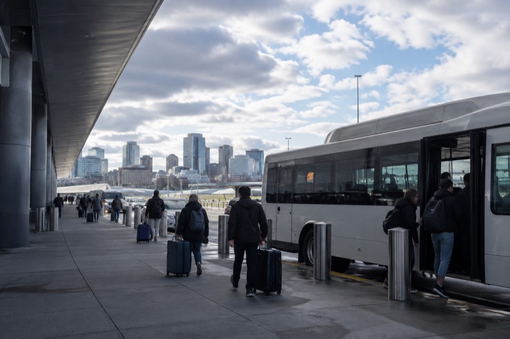 An airport terminal curb at Logan with a shuttle bus loading passengers